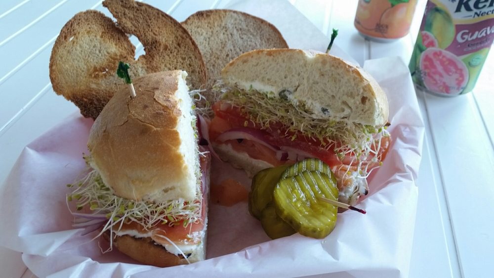 A stacked lox bagel sandwich from John's Bagel Deli with cream cheese, sprouts, tomato and red onion, served with pickles